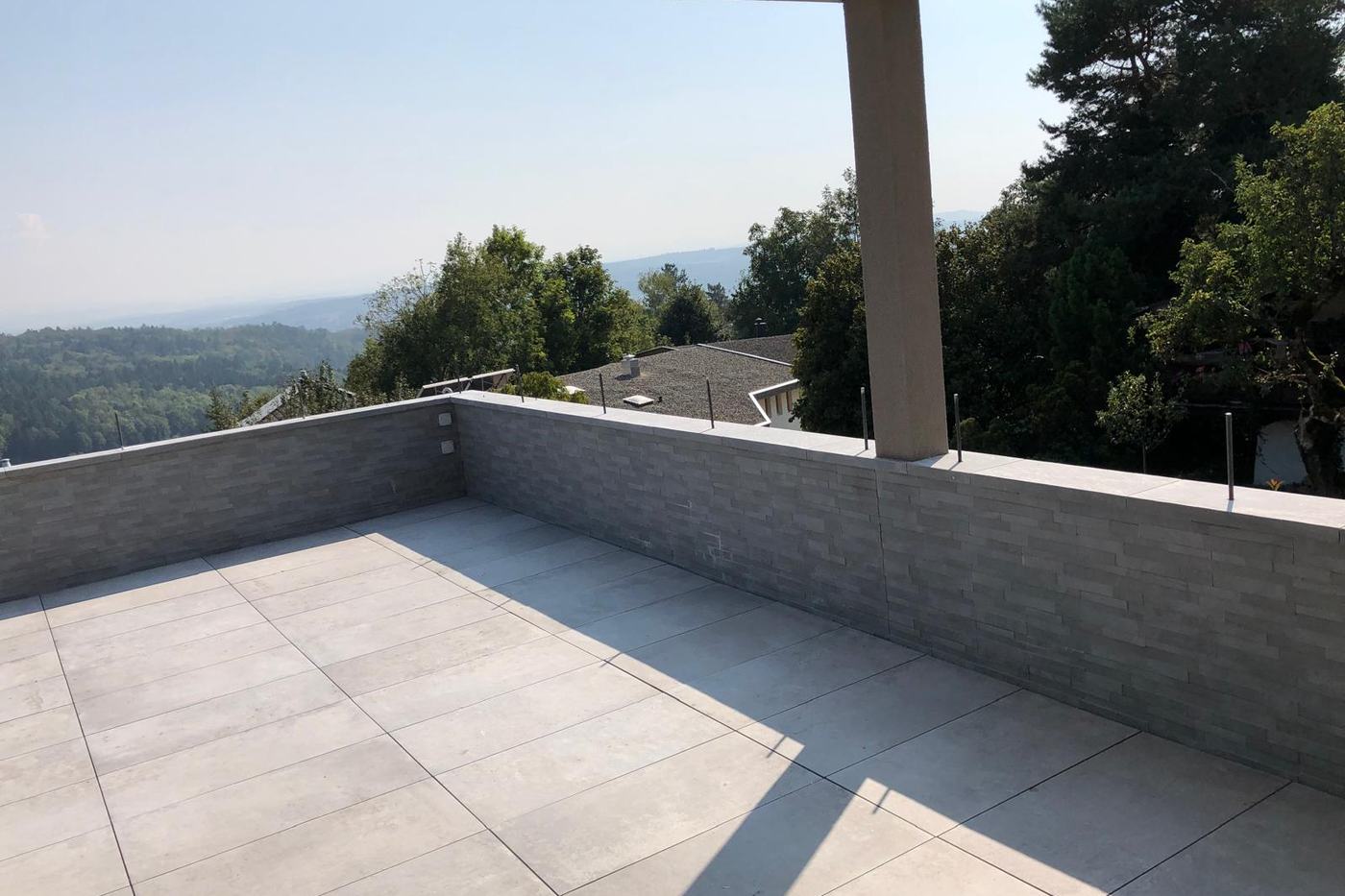 Fertige Dachterrasse mit grossformatigen Bodenplatten und verklinkerter Attika, Blick ins Grüne