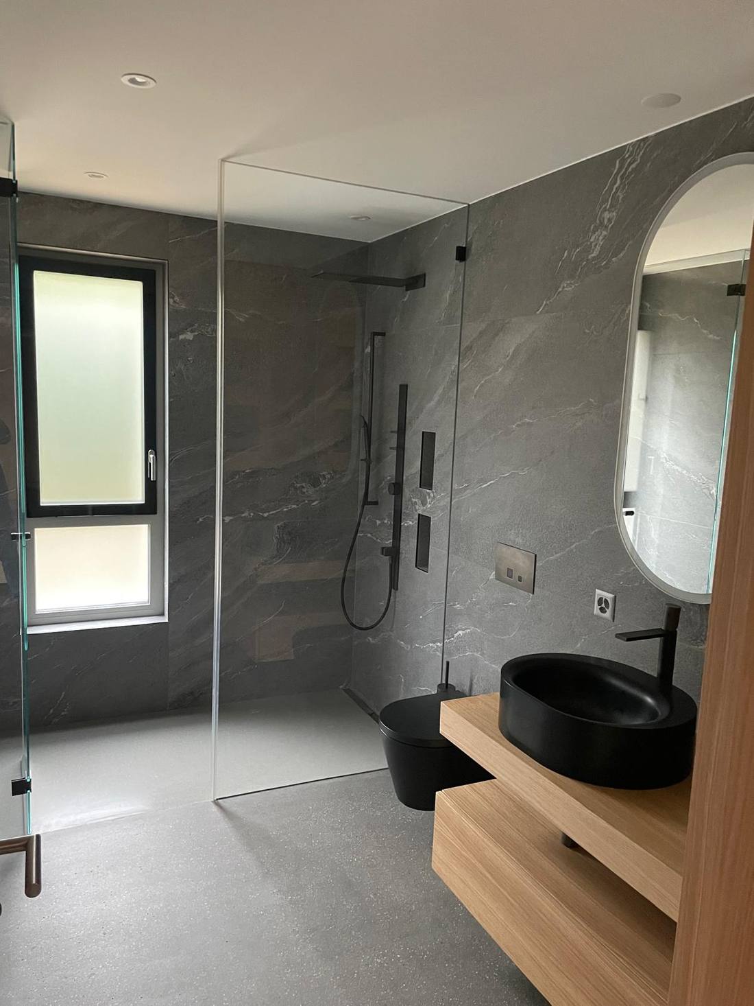 Fertige Dusche mit grossformatigem Feinsteinzeug, schwarzer Armatur und freistehendem Waschbecken