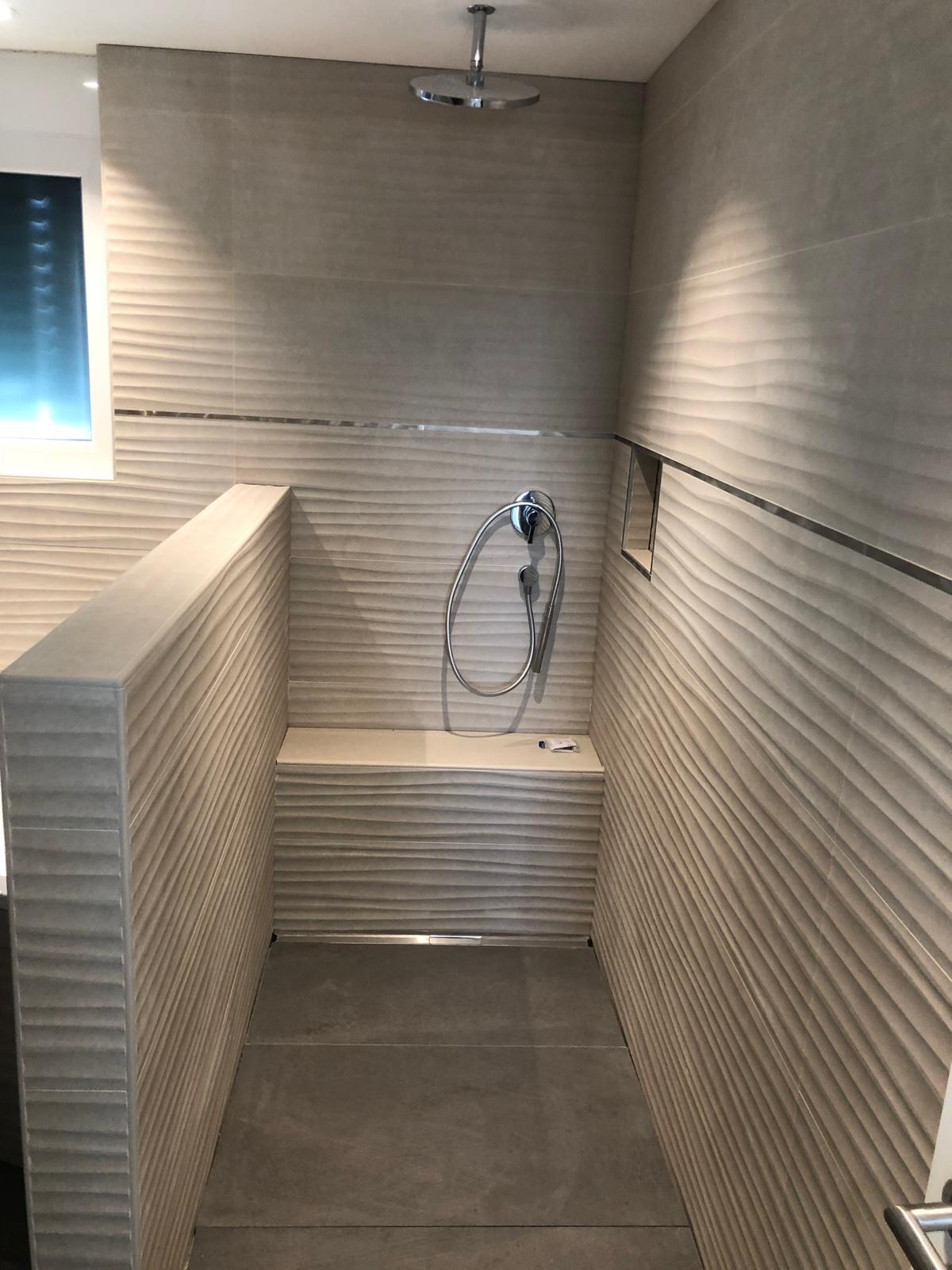 Ebenerdige Dusche mit gewellten Strukturfliesen, integrierter Sitzbank und Deckenbrause